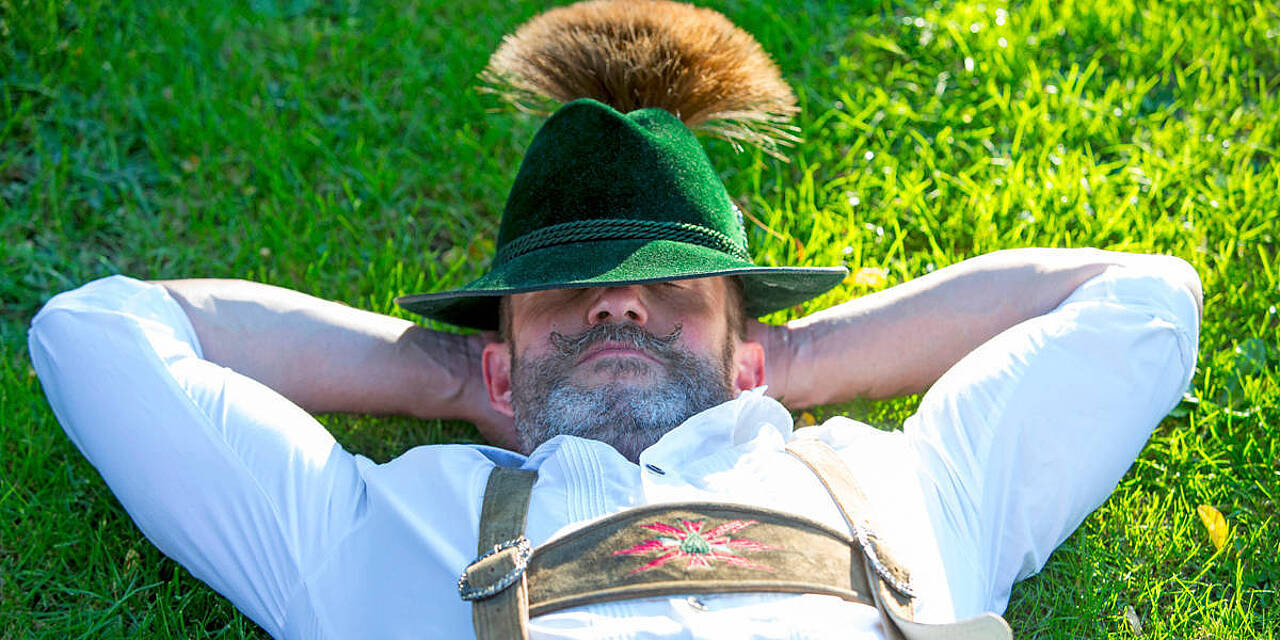 Ein Mann in einer bayerischen Lederhose liegt im Gras.