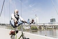 Ein älterer Mann auf dem Fahrrad hebt lachend seine Beine an.