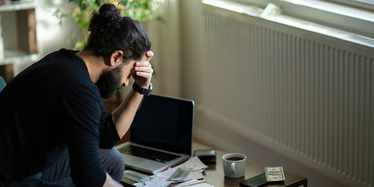 Junger Mann sitzt traurig und alleine vor Sofatisch mit Laptop