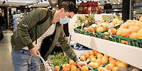 junger Mann mit Gesichtsmaske sucht Früchte im Supermarkt aus