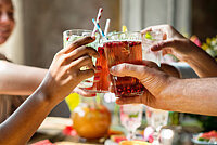 Vier Hände halten gefüllte Gläser mit Strohalmen in der Mitte zusammen, sodass sie sich berühren