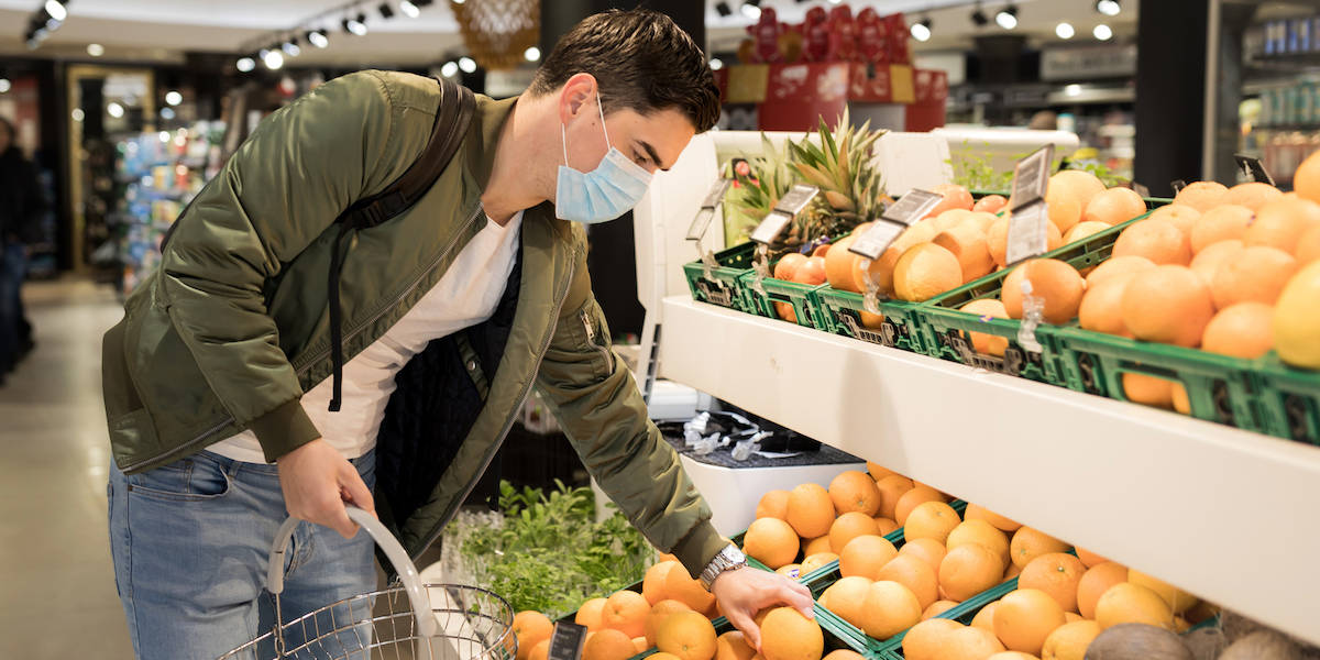 junger Mann mit Gesichtsmaske sucht Früchte im Supermarkt aus